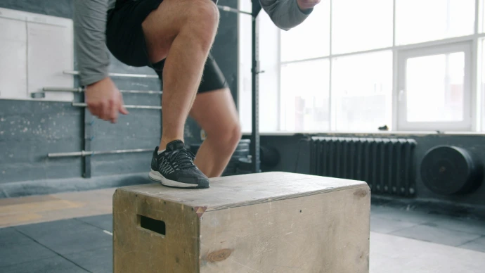 Man performing box jump exercise in gym.